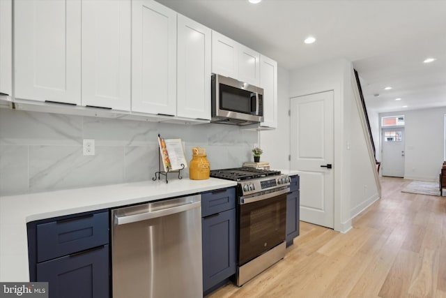 kitchen with blue cabinets, light wood-type flooring, white cabinets, stainless steel appliances, and backsplash