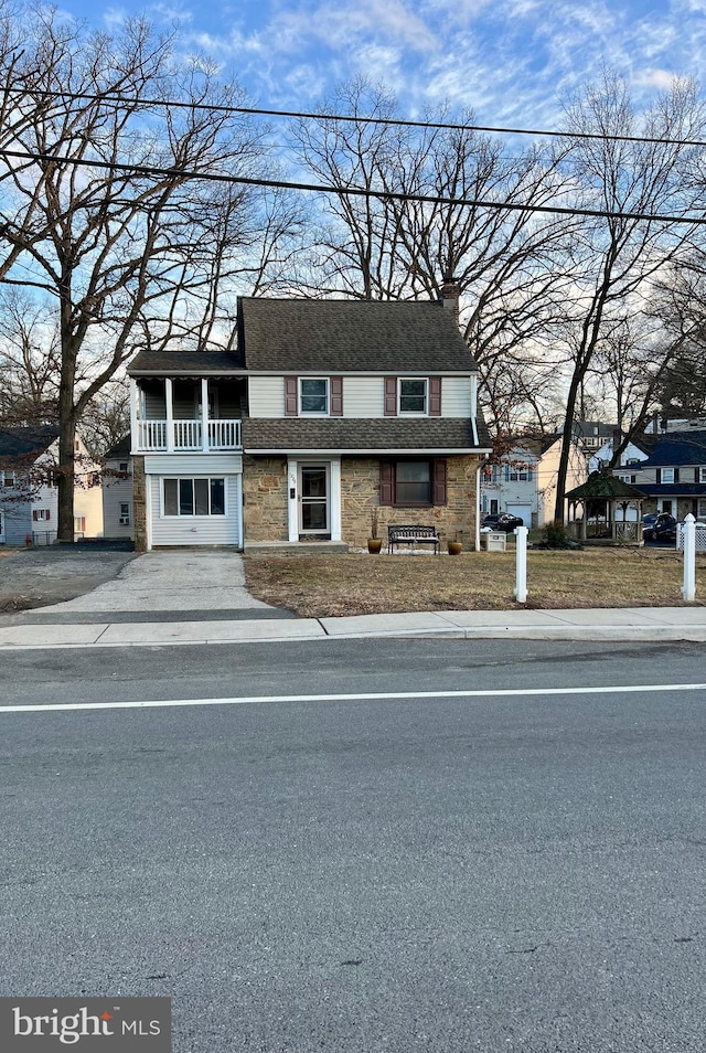 view of property featuring a balcony, stone siding, a chimney, and roof with shingles