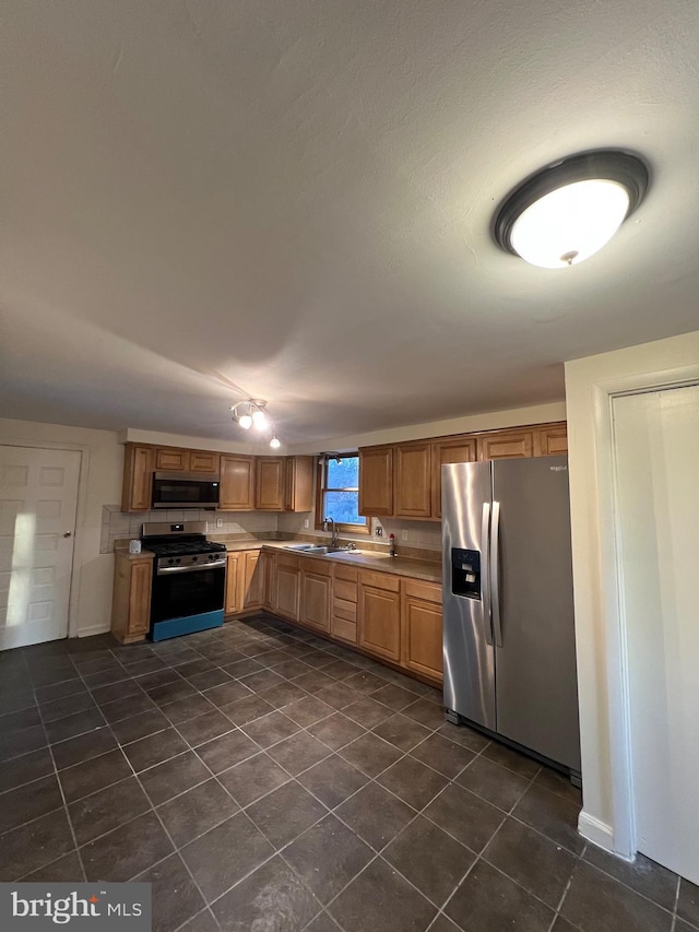 kitchen with appliances with stainless steel finishes, dark tile patterned flooring, and sink