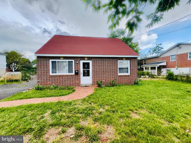view of front facade with a front yard, roof with shingles, and brick siding