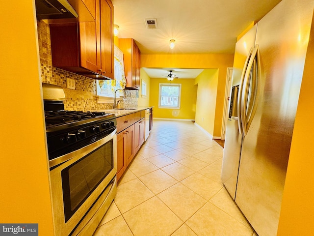 kitchen with appliances with stainless steel finishes, tasteful backsplash, brown cabinets, light tile patterned floors, and ceiling fan