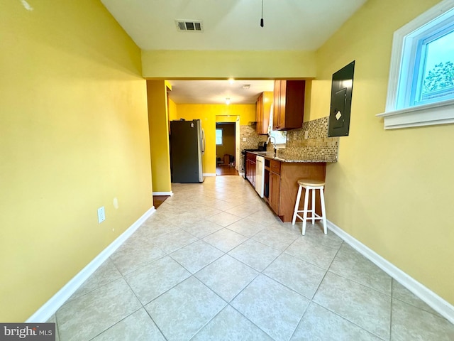 kitchen with freestanding refrigerator, tasteful backsplash, healthy amount of natural light, and light tile patterned floors