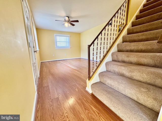 stairway featuring wood finished floors, a ceiling fan, and baseboards
