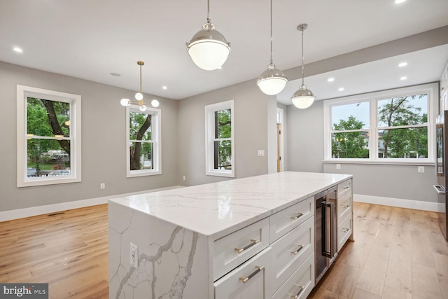 kitchen with hanging light fixtures, white cabinetry, a kitchen island, and light stone counters