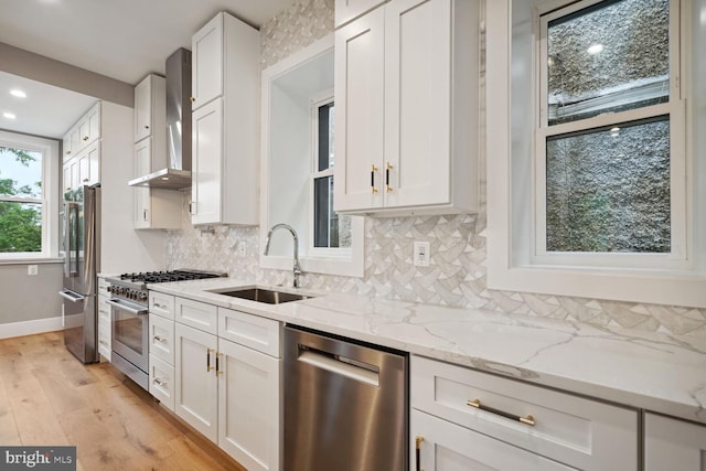 kitchen featuring wall chimney exhaust hood, sink, high quality appliances, light stone countertops, and white cabinets