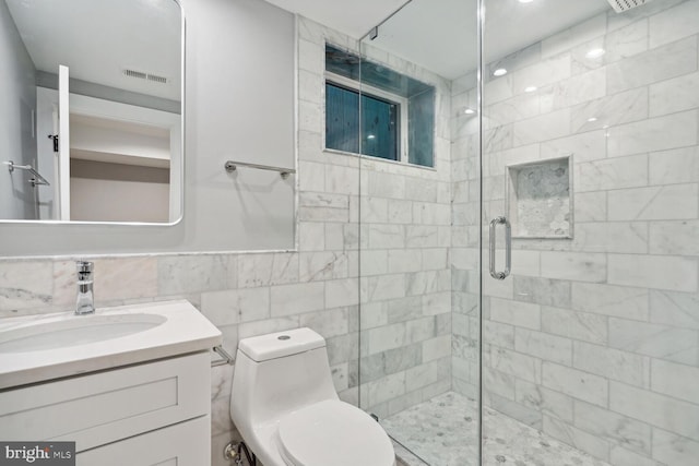 bathroom with vanity, a shower with shower door, tile walls, and toilet