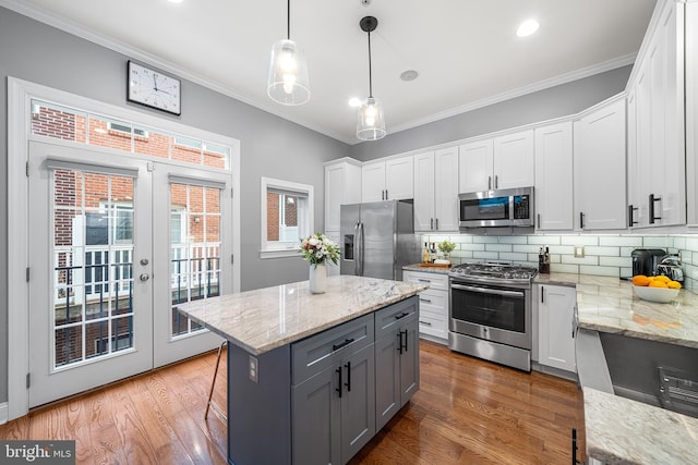 kitchen with stainless steel appliances, crown molding, white cabinets, and decorative light fixtures