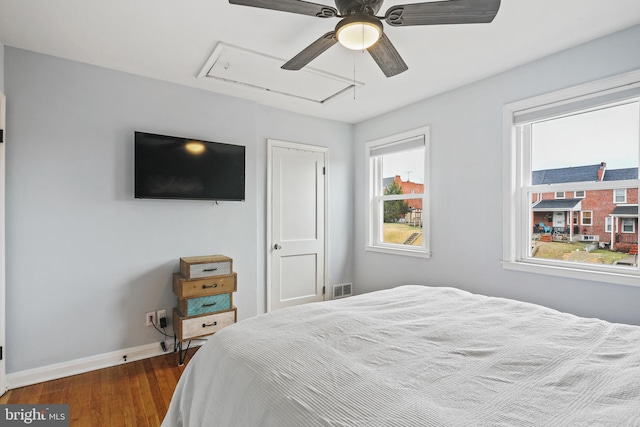 bedroom featuring visible vents, a ceiling fan, baseboards, dark wood finished floors, and attic access