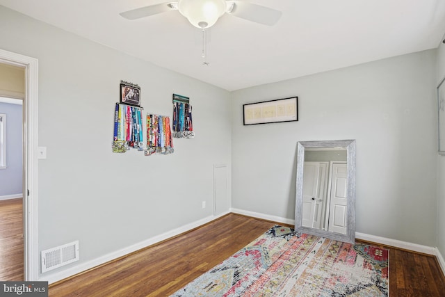 empty room featuring a ceiling fan, visible vents, baseboards, and wood finished floors