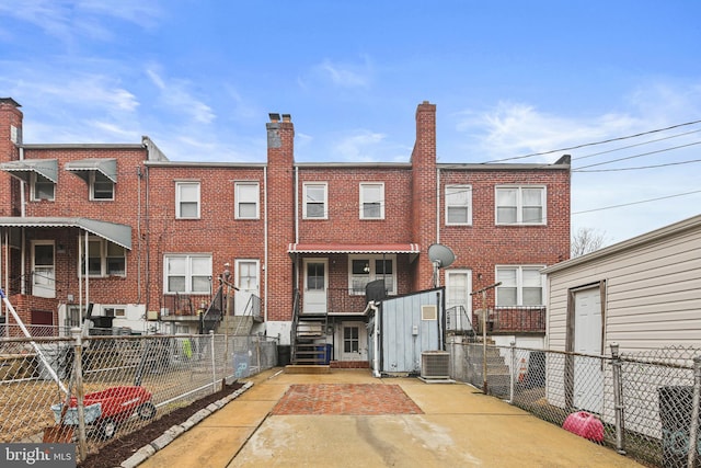 rear view of property with central air condition unit, brick siding, fence, and entry steps