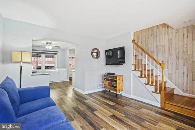 living area featuring baseboards, arched walkways, a ceiling fan, stairway, and wood finished floors