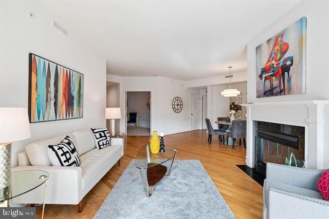 living room featuring a fireplace with flush hearth, visible vents, and wood finished floors