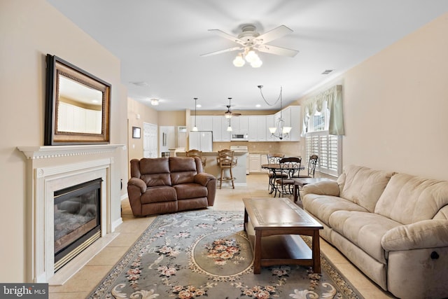 tiled living room with a fireplace and ceiling fan with notable chandelier