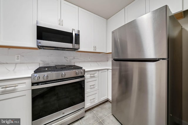 kitchen featuring light tile patterned flooring, appliances with stainless steel finishes, tasteful backsplash, white cabinets, and light stone countertops