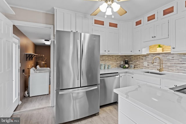 kitchen with appliances with stainless steel finishes, light stone countertops, washer and clothes dryer, sink, and white cabinetry