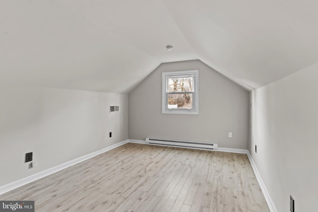 additional living space with light wood-type flooring, vaulted ceiling, and a baseboard radiator