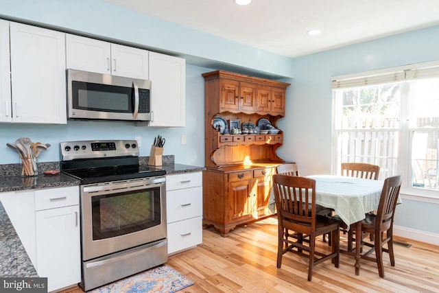 kitchen featuring dark stone countertops, appliances with stainless steel finishes, light wood-type flooring, and white cabinets