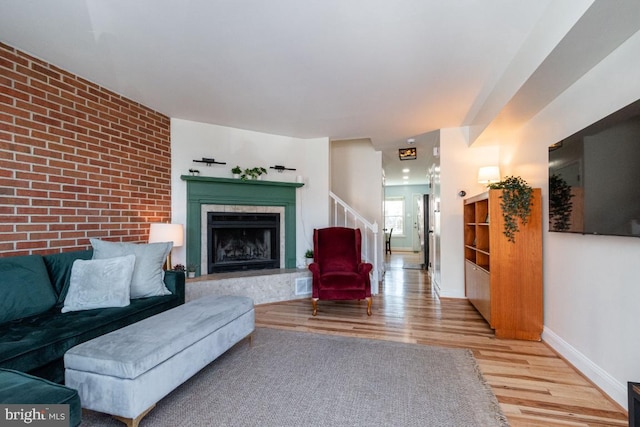 living room with brick wall, a high end fireplace, baseboards, stairs, and light wood-type flooring