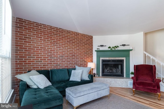 living area featuring a fireplace, brick wall, and wood finished floors