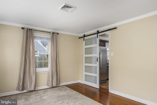 spare room with ornamental molding, a barn door, and dark hardwood / wood-style floors