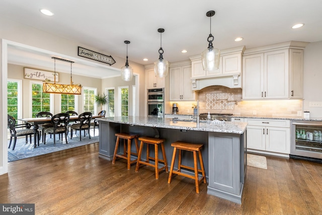 kitchen with light stone countertops, pendant lighting, a center island with sink, and beverage cooler