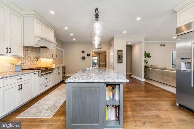 kitchen featuring white cabinetry, light stone counters, pendant lighting, stainless steel appliances, and a kitchen island with sink