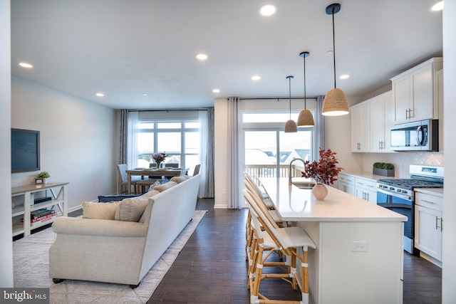 kitchen featuring a breakfast bar area, white cabinetry, hanging light fixtures, stainless steel appliances, and a kitchen island with sink