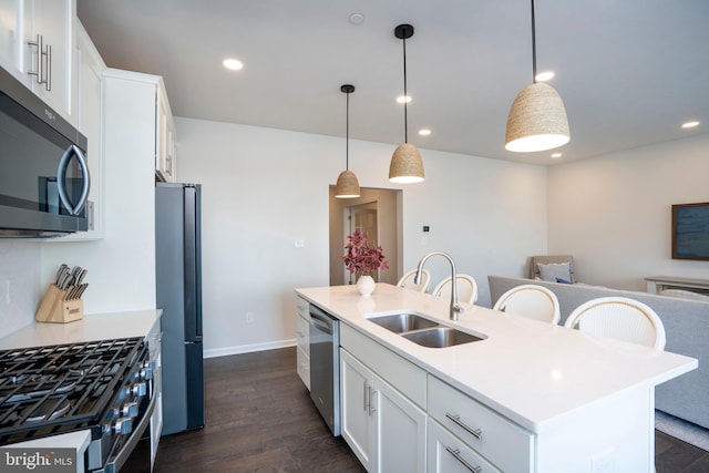 kitchen featuring sink, stainless steel appliances, white cabinets, a center island with sink, and decorative light fixtures