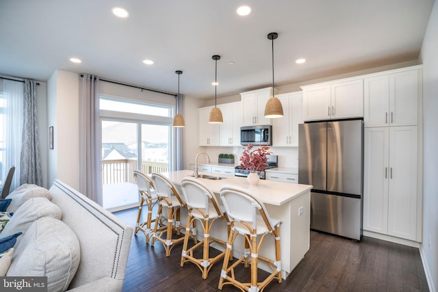 kitchen featuring sink, decorative light fixtures, appliances with stainless steel finishes, a kitchen island with sink, and white cabinets