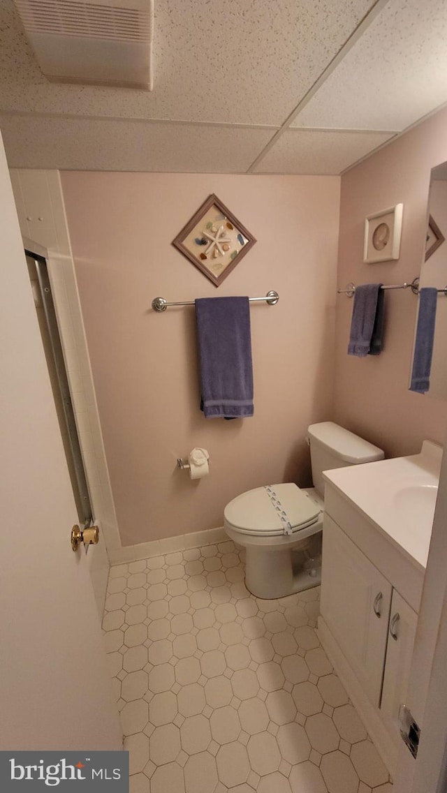 bathroom with a drop ceiling, toilet, vanity, and baseboards