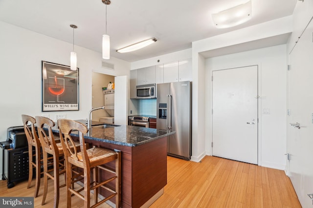 kitchen featuring light wood finished floors, appliances with stainless steel finishes, white cabinetry, pendant lighting, and a sink