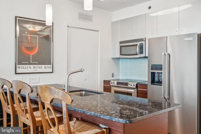 kitchen featuring brown cabinetry, white cabinets, appliances with stainless steel finishes, hanging light fixtures, and a sink