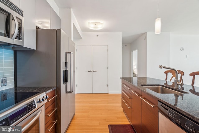 kitchen with a sink, appliances with stainless steel finishes, dark stone counters, modern cabinets, and pendant lighting