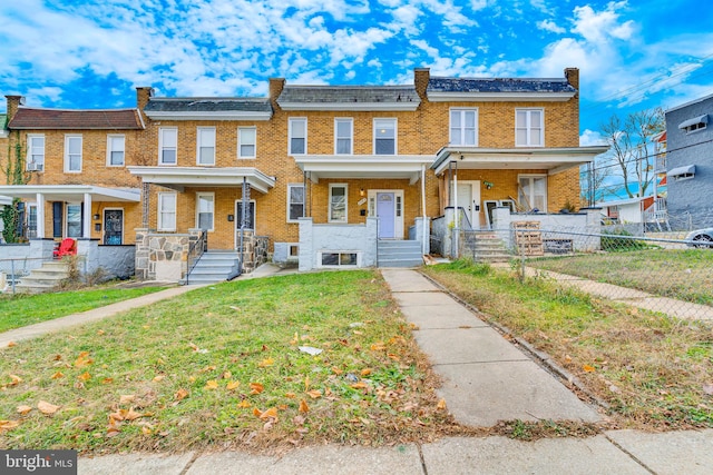 townhome / multi-family property with covered porch, a fenced front yard, a front yard, and brick siding