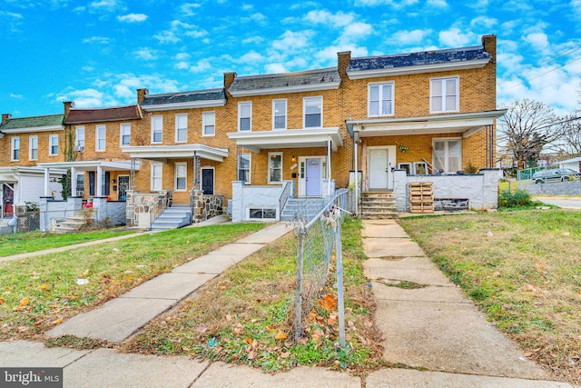 townhome / multi-family property with covered porch, a fenced front yard, a front yard, and brick siding