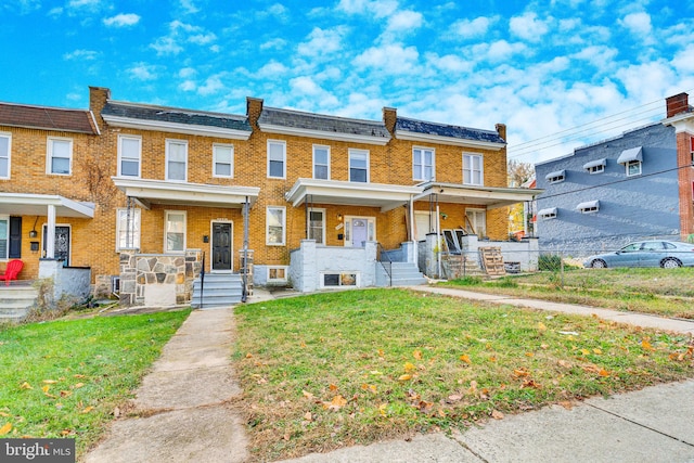 townhome / multi-family property featuring covered porch, brick siding, and a front lawn