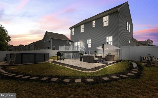 back house at dusk featuring an outdoor hangout area, a lawn, a patio, and a swimming pool side deck