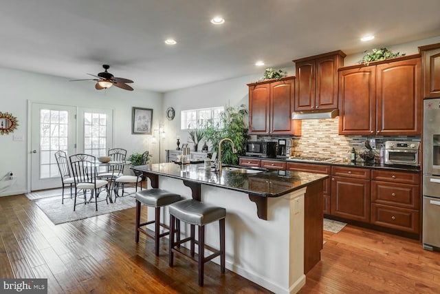 kitchen with wood-type flooring, sink, an island with sink, and dark stone countertops