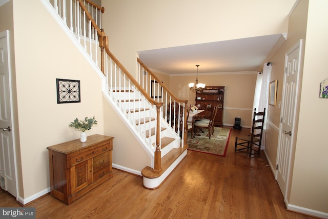 stairs with crown molding, a towering ceiling, wood-type flooring, and a notable chandelier