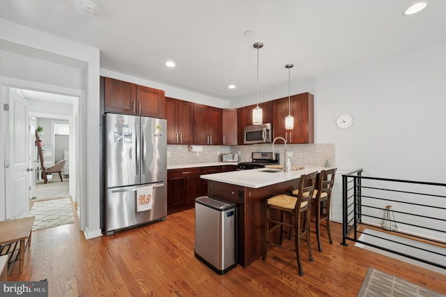 kitchen with pendant lighting, stainless steel appliances, light countertops, a peninsula, and a kitchen breakfast bar