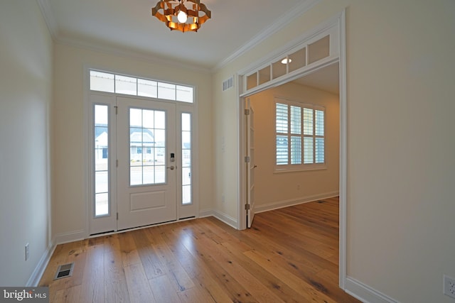 foyer entrance with hardwood / wood-style flooring, baseboards, visible vents, and ornamental molding