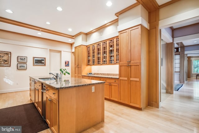 kitchen featuring an island with sink, sink, ornamental molding, light stone counters, and light wood-type flooring