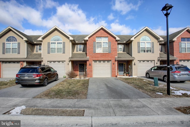 townhome / multi-family property featuring driveway, brick siding, an attached garage, and a shingled roof