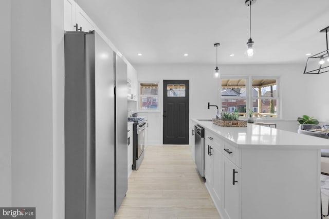 kitchen with sink, stainless steel appliances, white cabinets, hanging light fixtures, and a kitchen island with sink