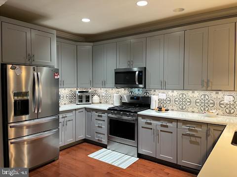 kitchen with gray cabinets, tasteful backsplash, appliances with stainless steel finishes, and hardwood / wood-style flooring