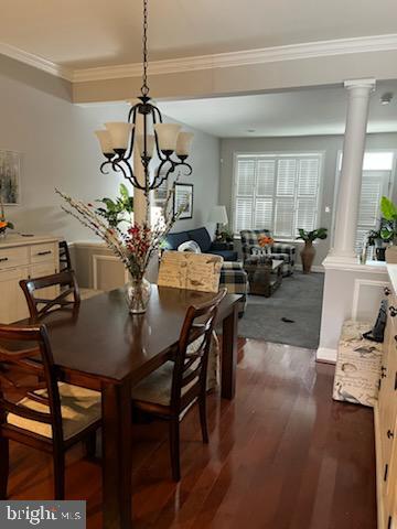 dining area featuring dark hardwood / wood-style flooring, a notable chandelier, ornamental molding, and ornate columns