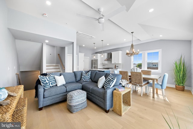 living area with light wood-type flooring, vaulted ceiling, stairway, and ceiling fan with notable chandelier