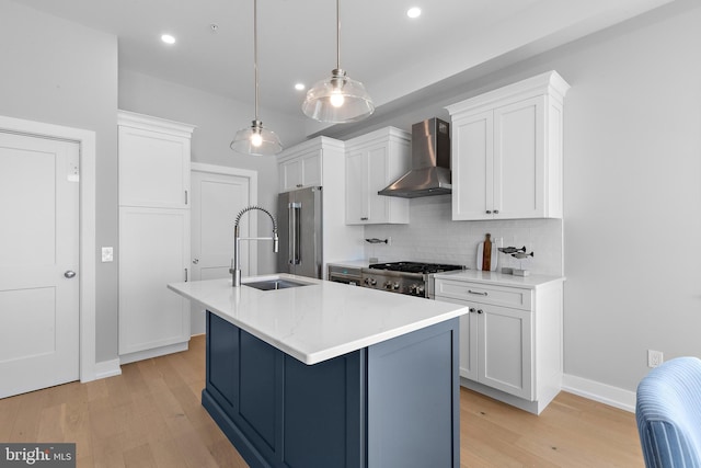 kitchen with wall chimney exhaust hood, high quality fridge, stove, light wood-style floors, and a sink