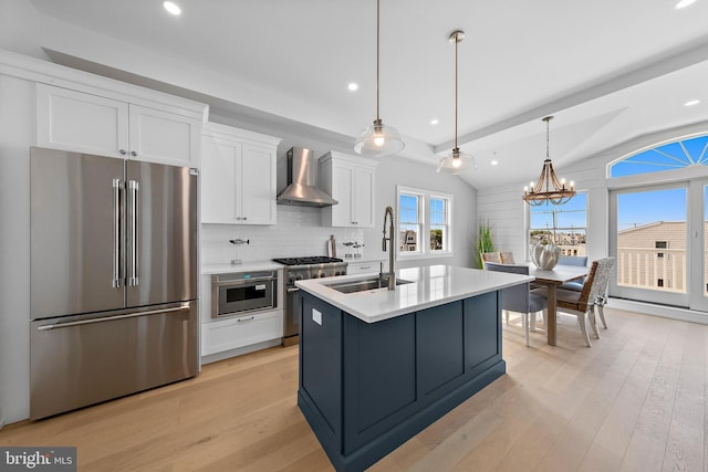 kitchen with tasteful backsplash, high quality appliances, wall chimney range hood, white cabinetry, and a sink