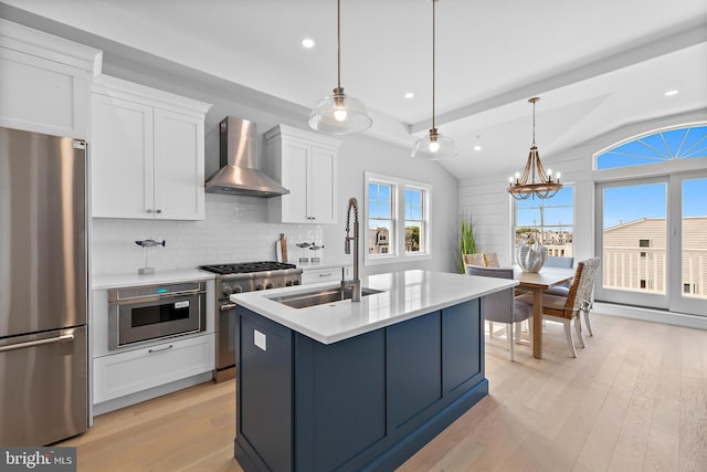 kitchen featuring wall chimney range hood, light wood-style flooring, appliances with stainless steel finishes, and a sink